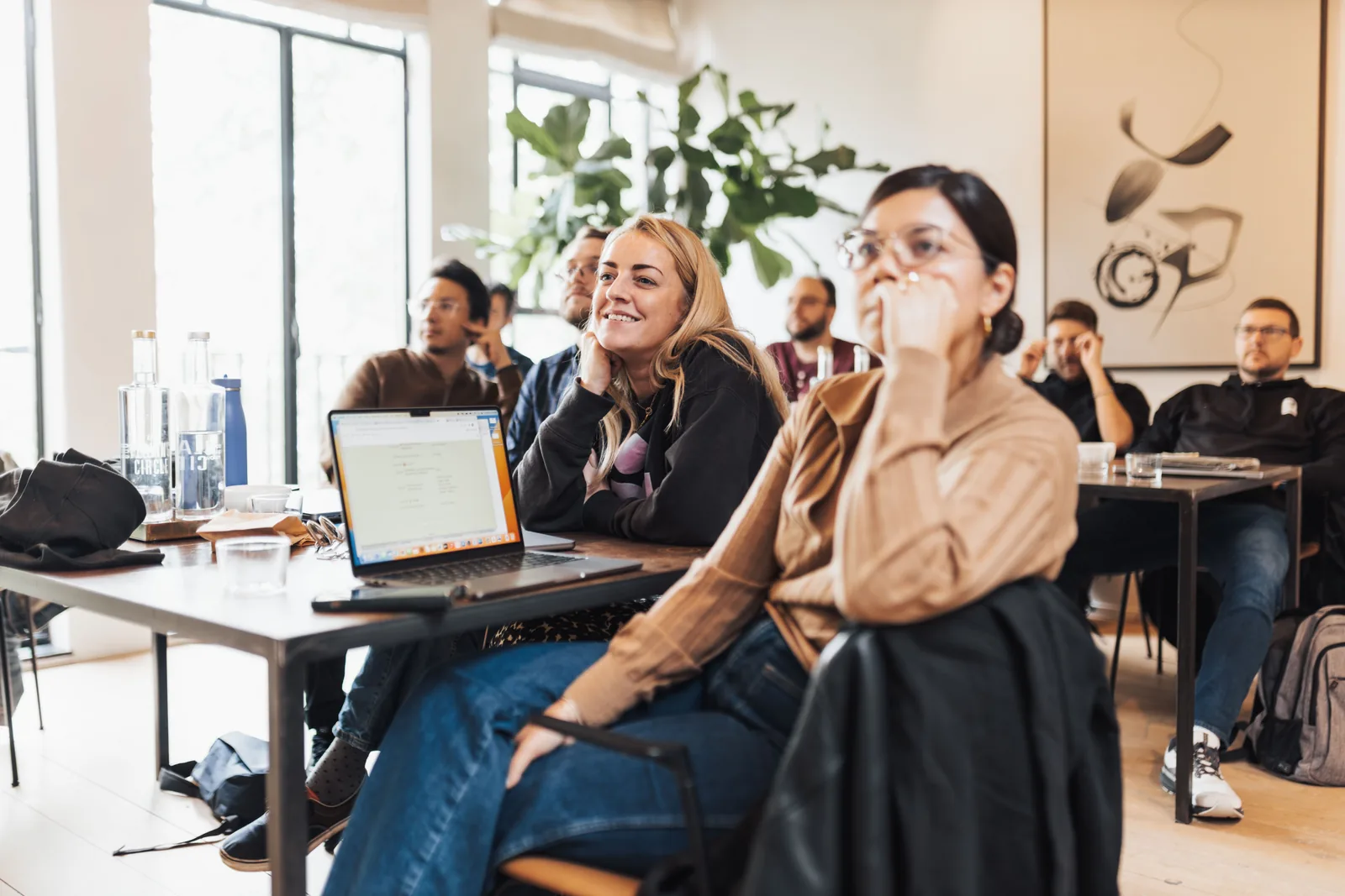 Deelnemers aan een training in een lichte werkruimte, met laptops op tafel