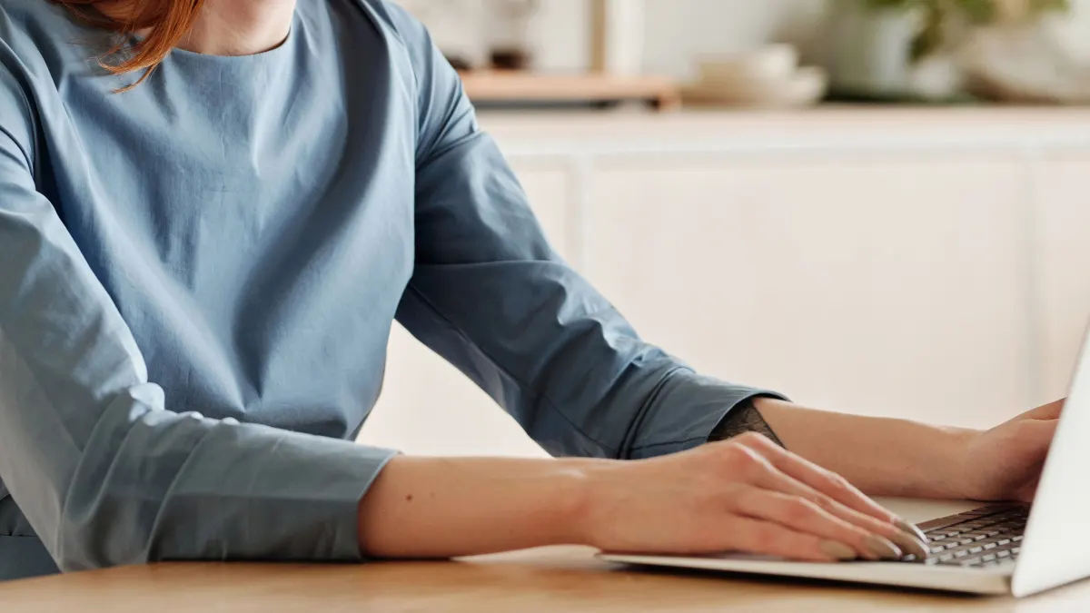 Handen op een laptop aan een houten bureau in een licht kantoor
