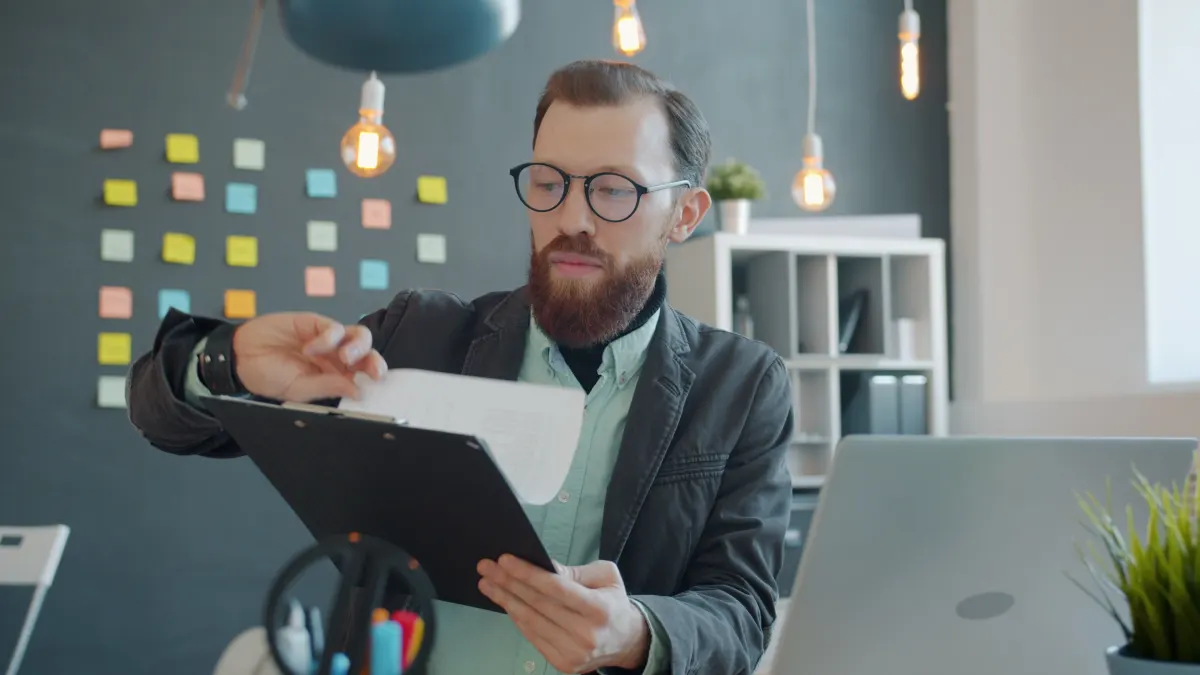 Man met een klembord vergelijkt twee documenten aan zijn bureau